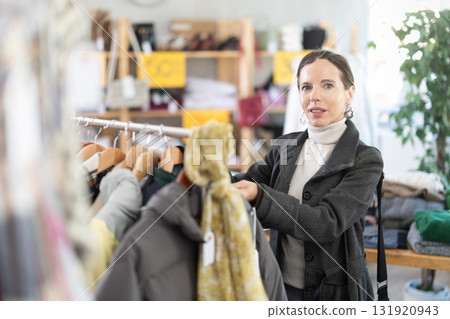 Glad middle-aged woman choosing something for autumn-winter in clothing store 131920943