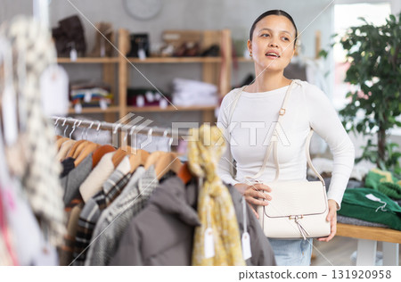 Young asian woman trying on elegant handbag made of high-quality material in clothes and accessories shop 131920958