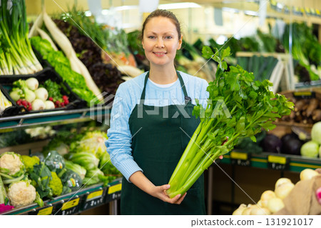 Smiling female merchandiser with celery in hands in grocery supermarket 131921017