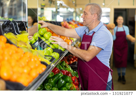 Aged salesman putting apples on food stall in grocery store 131921077