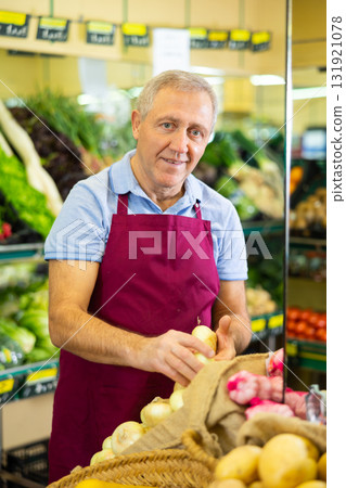 Professional old male seller putting onion on shelves in grocery shop Professional old male seller putting onion on shelves in grocery shop 131921078