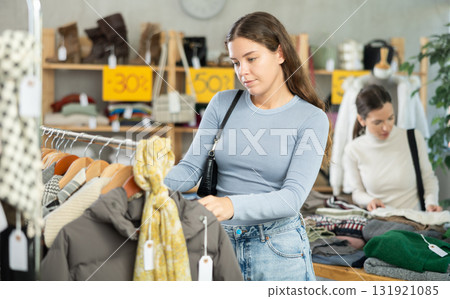 Young woman chooses different winter clothes in clothing store Young woman chooses different winter clothes in clothing store 131921085