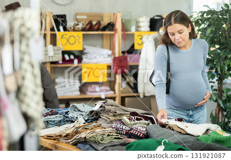 Pregnant woman choosing sweater in clothing store Pregnant woman choosing sweater in clothing store 131921087