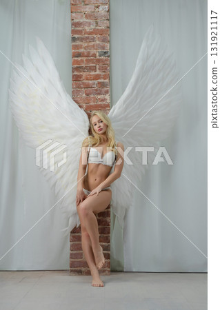 Beautiful woman with angel wings poses in studio setting Beautiful woman with angel wings poses in studio setting 131921117