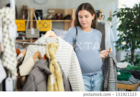 Pregnant woman choosing down jacket in clothing store 131921123