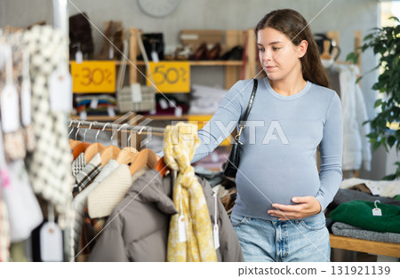 Pregnant woman chooses fashionable dress for autumn-winter season in clothing store Pregnant woman chooses fashionable dress for autumn-winter season in clothing store 131921139