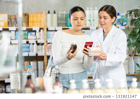 Positive asian woman client choosing liquid syrup and scan QR code on label at pharmacy, young woman pharmacist consulting customer 131921147