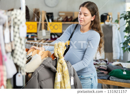 Pregnant woman choosing outerwear in clothing store 131921157