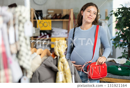 Pregnant woman chooses fashionable handbag in clothing store 131921164