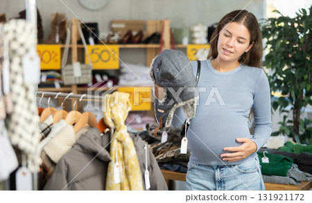 Pregnant woman choosing fur hat in clothing store 131921172