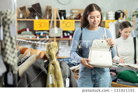 Happy girl chooses fashionable bag in clothing store Happy girl chooses fashionable bag in clothing store 131921191