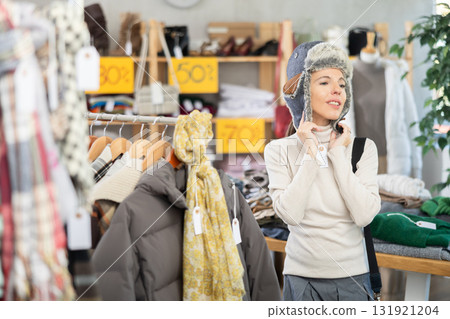 Female shopper chooses a fur hat in clothing store 131921204