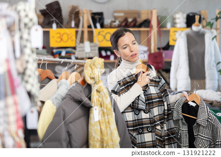 Woman chooses checkered jacket searches for fashionable clothes in clothing boutique Woman chooses checkered jacket searches for fashionable clothes in clothing boutique 131921222