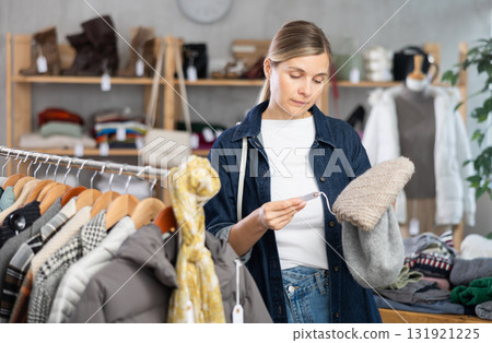 Focused european young woman choose hat for autumn-winter season in clothing store Focused european young woman choose hat for autumn-winter season in clothing store 131921225