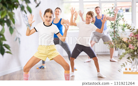 Joyful sister and brother practicing expressive dance movements against backdrop of mom and dad training together in wellness center 131921264