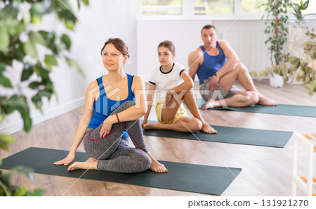 School children and their parents exercising on mats in Lord of the Fishes Pose, or Matsyendrasana during family yoga training in gym fitness center indoors 131921270