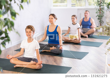 Happy preteen boy practicing lotus pose of yoga with his family 131921273