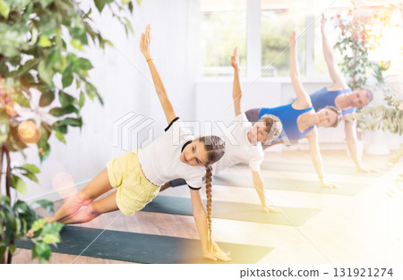 Kids and parents practicing Side Plank Pose or Vasisthasana on mats during family Hatha yoga class in studio 131921274