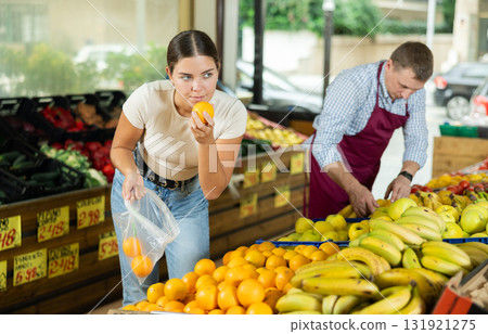 Young female shopper selects and buys fresh oranges in supermarket 131921275