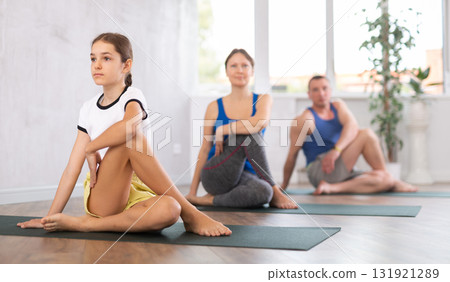 Middle-aged woman, man, teenage girl and boy practicing Lord of the Fishes Pose, or Matsyendrasana on mats during family Hatha yoga class in wellness studio Middle-aged woman, man, teenage girl and boy practicing Lord of the Fishes Pose, or Matsyendrasana on mats during family Hatha yoga class in wellness studio 131921289