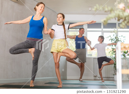 Friendly sporty parents with preteen daughter and son balancing in Vrikshasana or Tree position on gymnastic mats barefoot in yoga studio Friendly sporty parents with preteen daughter and son balancing in Vrikshasana or Tree position on gymnastic mats barefoot in yoga studio 131921290