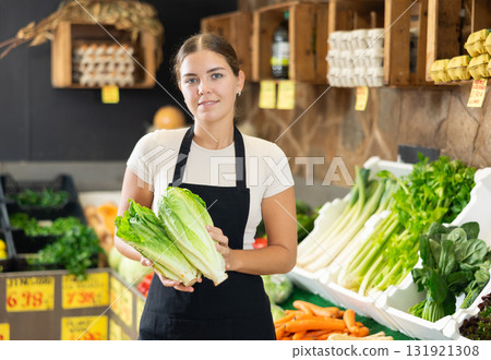 Young female seller in apron displaying assortment of lettuce buds at supermarket 131921308