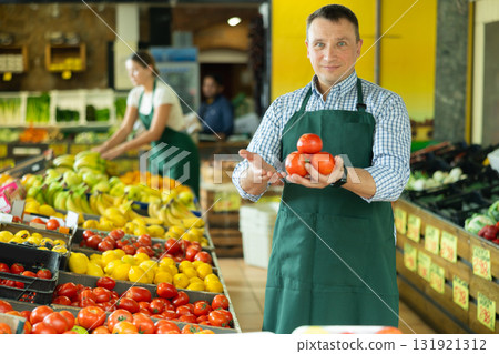 Male seller of vegetable department of store replenishing showcase with tomato, put ones on showcase 131921312