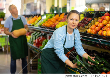 Positive middle-aged woman, skilled market assistant arranging organic cucumber on shelves in hypermarket Positive middle-aged woman, skilled market assistant arranging organic cucumber on shelves in hypermarket 131921321