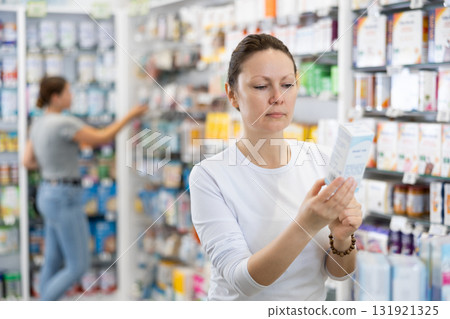 Young female shopper carefully chooses cosmetics in pharmacy Young female shopper carefully chooses cosmetics in pharmacy 131921325