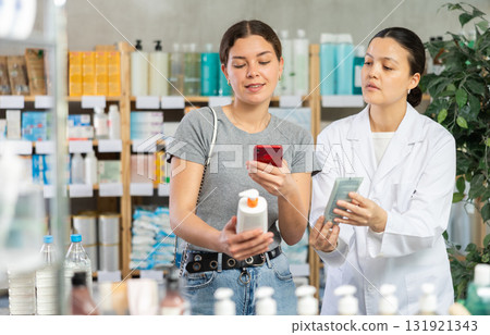 Young girl choosing cream or skin care product in pharmacy and scan QR code on label, young asian woman pharmacist consulting and offering variety of goods to customer 131921343