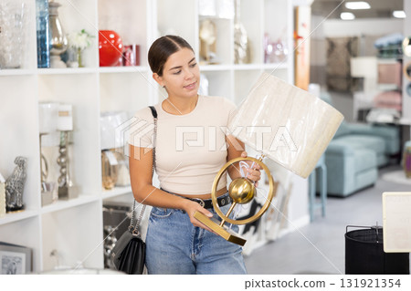 Smiling female purchaser choosing stylish table lamp in shop 131921354