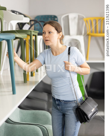 Interested woman looking for new chairs in furniture store 131921396