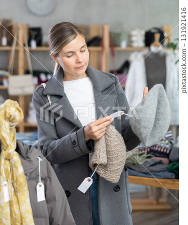 Focused european young woman choose hat for autumn-winter season in clothing store Focused european young woman choose hat for autumn-winter season in clothing store 131921416