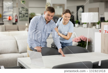 Adult man and woman choosing dining table in furniture store 131921418