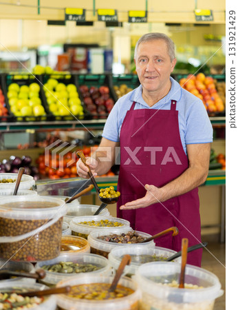 Elderly salesman showing olives in grocery store Elderly salesman showing olives in grocery store 131921429