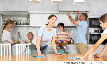 Friendly large family cleans room together. Mom and daughter are dusting table. Son is vacuuming oom. Father together with daughters wipe dust 131921452