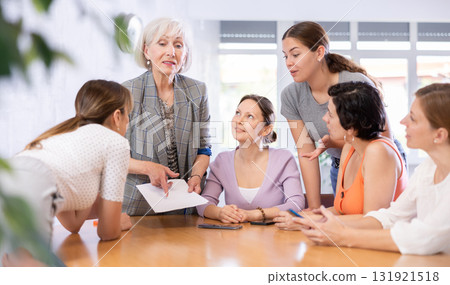 Women discuss documents sitting at table in office Women discuss documents sitting at table in office 131921518