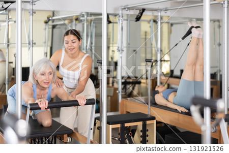 Aged woman practicing pilates on reformer with young female trainer Aged woman practicing pilates on reformer with young female trainer 131921526