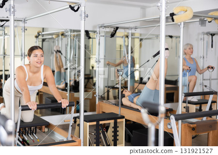 Positive young girl practicing pilates stretching exercises on reformer at gym 131921527