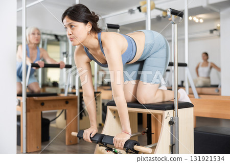 Young positive woman doing Pilates on special equipment in gym Young positive woman doing Pilates on special equipment in gym 131921534