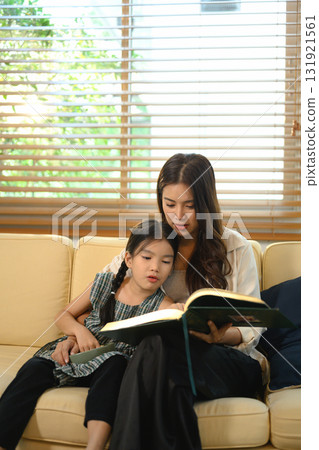 Happy Asian mother and little girl enjoying story time on the sofa, sharing smiles, love, and family togetherness 131921561