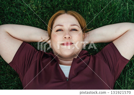 Beautiful plus size woman lying on grass after outdoors training session. Beautiful plus size woman lying on grass after outdoors training session. 131921570
