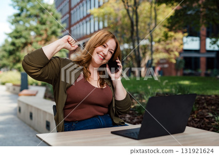 Plus size woman working remotely from coffee shop, making phone call with client. Plus size woman working remotely from coffee shop, making phone call with client. 131921624