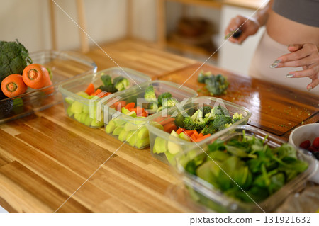 Healthy meal prep containers filled with fresh vegetables on a wooden kitchen counter Healthy meal prep containers filled with fresh vegetables on a wooden kitchen counter 131921632