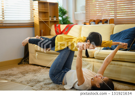 Happy mother playing airplane game with her daughter at home, lifting the child with her legs Happy mother playing airplane game with her daughter at home, lifting the child with her legs 131921634