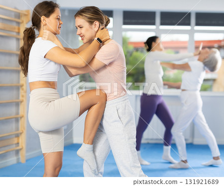 Young woman practicing knee strike to sparring female partner stomach in self-defense training 131921689
