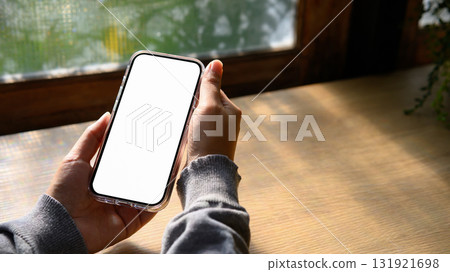 Person holding empty screen smartphone over kitchen counter in natural morning light Person holding empty screen smartphone over kitchen counter in natural morning light 131921698
