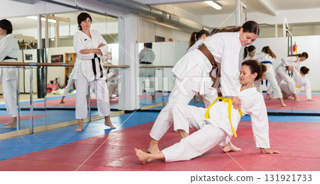 Womens practicing new karate moves in pairs in class with trainer 131921733