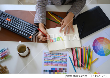 Designer sketching logo with colored pencils in notebook at bright office desk 131921739