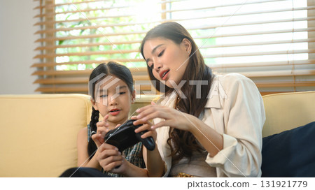Parent and daughter spending quality time together, learning and playing video games 131921779